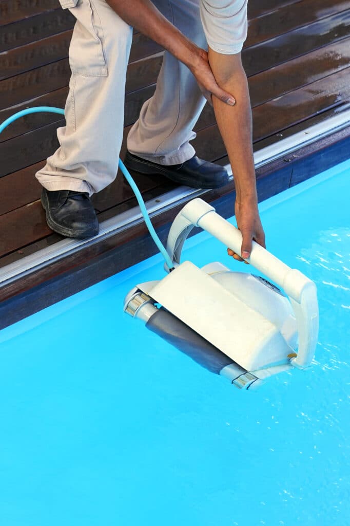 Installation robot nettoyeur piscine automatique eau bleue Homme en pantalon beige et chaussures noires installant un robot nettoyeur de piscine automatique dans l'eau bleue.